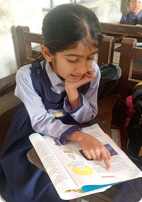 A young girl reading a book at her school desk