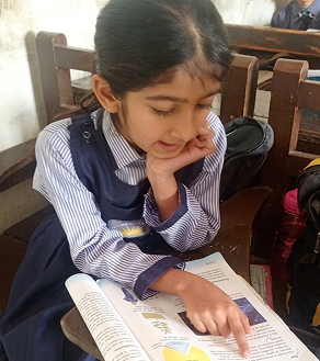 A young girl reading a book at her school desk